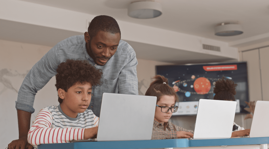 teacher helping students looking at comouter screen